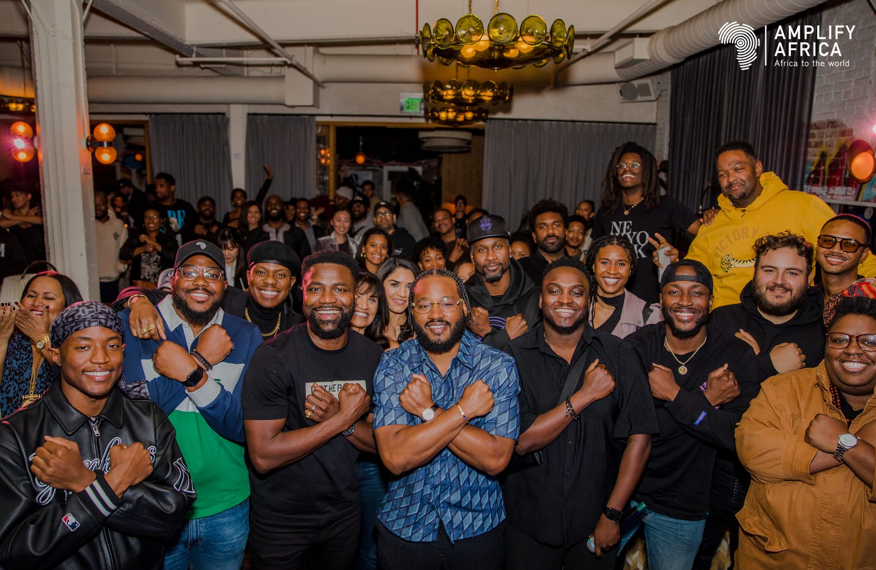 Amplify Africa community members crossing their arms in the Wakanda salute at a gathering
