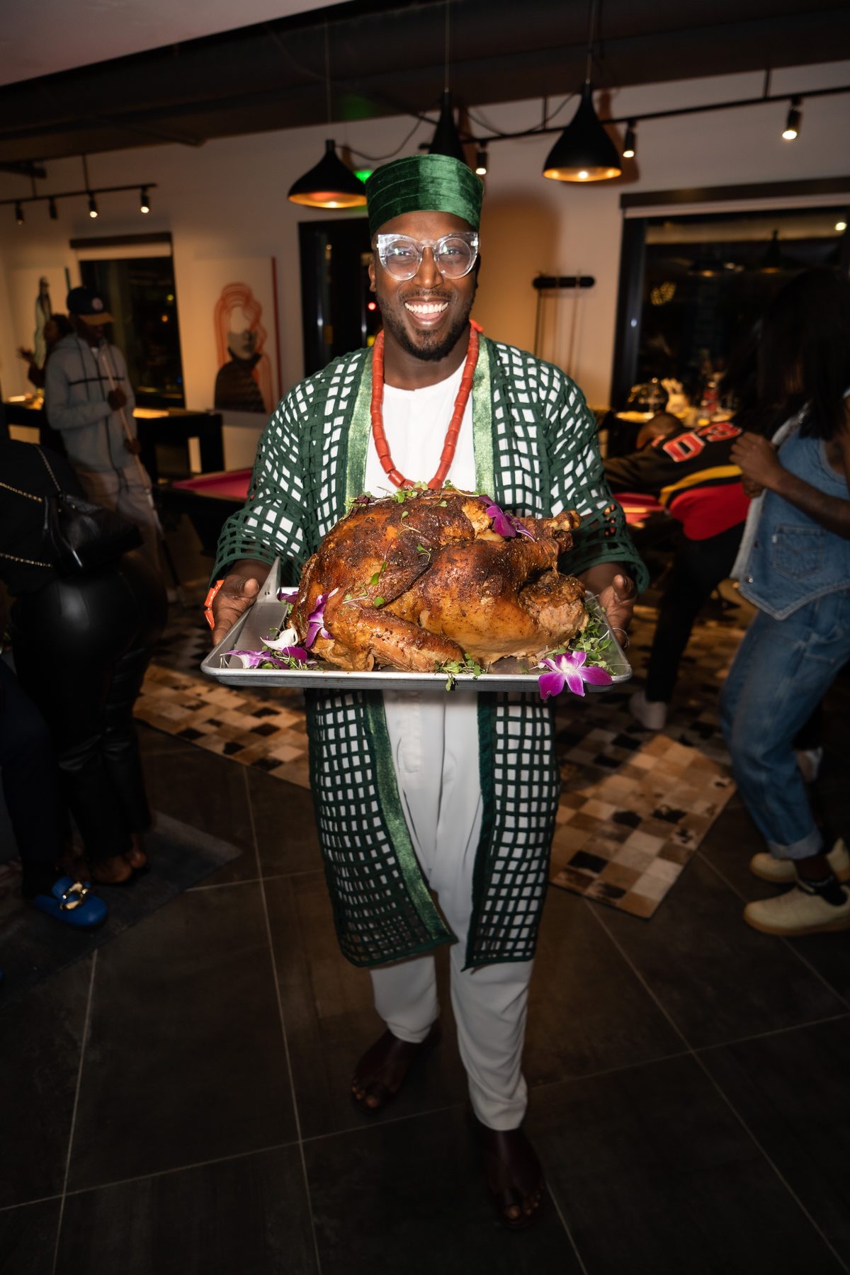 Host in traditional attire serving a roast turkey at an Amplify Africa Friendsgiving
